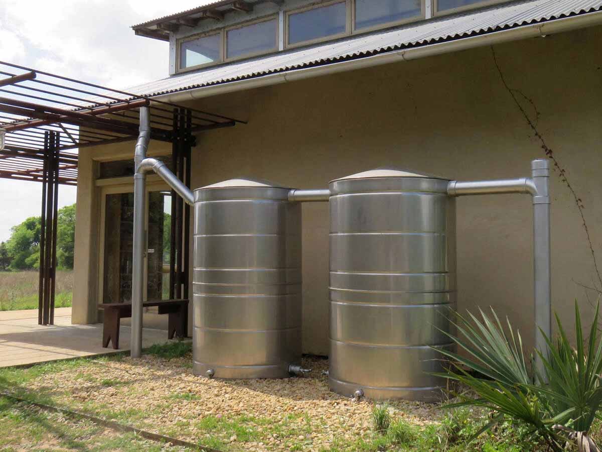 Two Texas Metal Tanks stainless steel rainwater tanks connected by piping next to a building